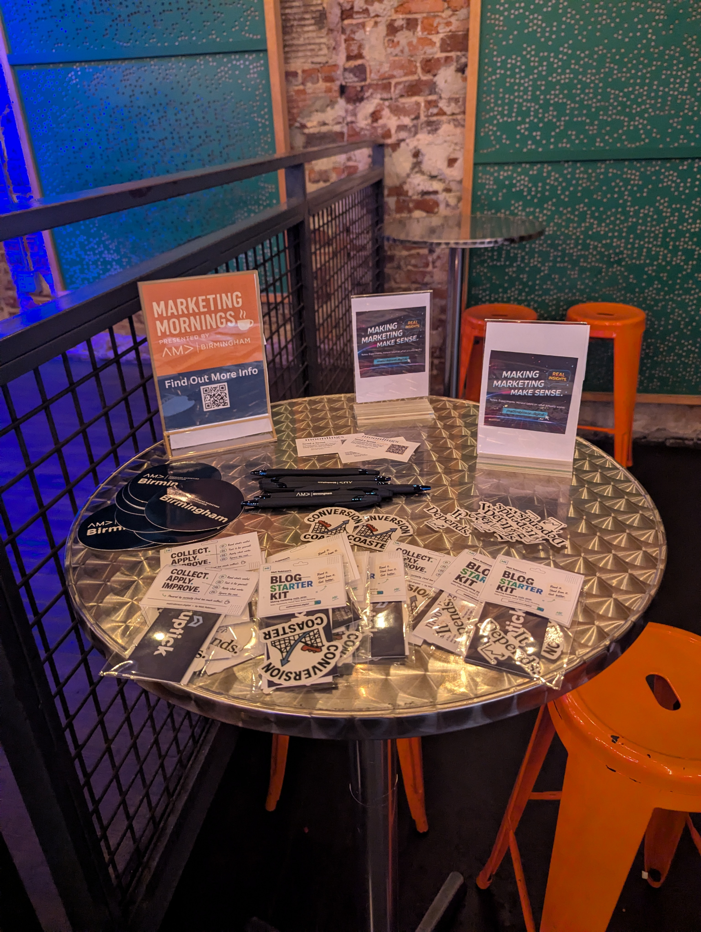 A table of Marketing Mornings signage, stickers, pens and Blog Starter Kit cards at the event