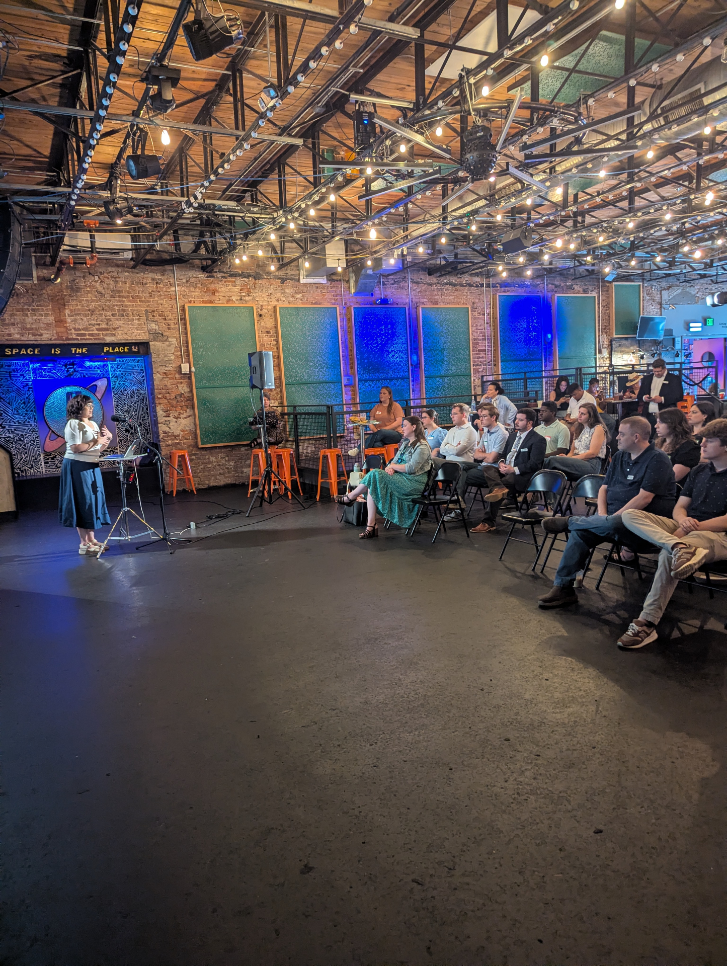 A speaker addressing a seated audience at The Localist Lab inside Saturn in Birmingham