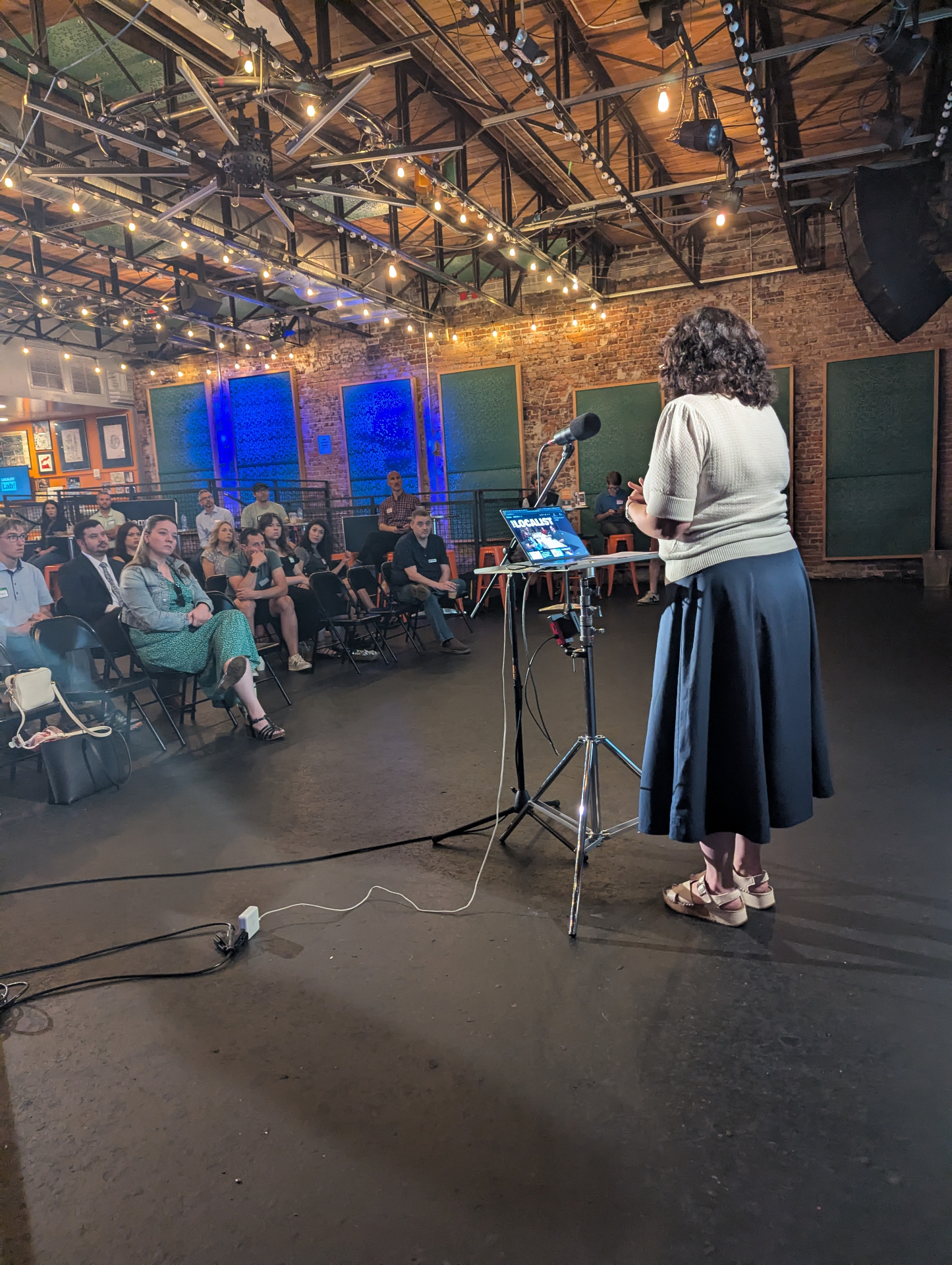 View from behind the stage of a speaker presenting to the Localist Lab audience at Saturn